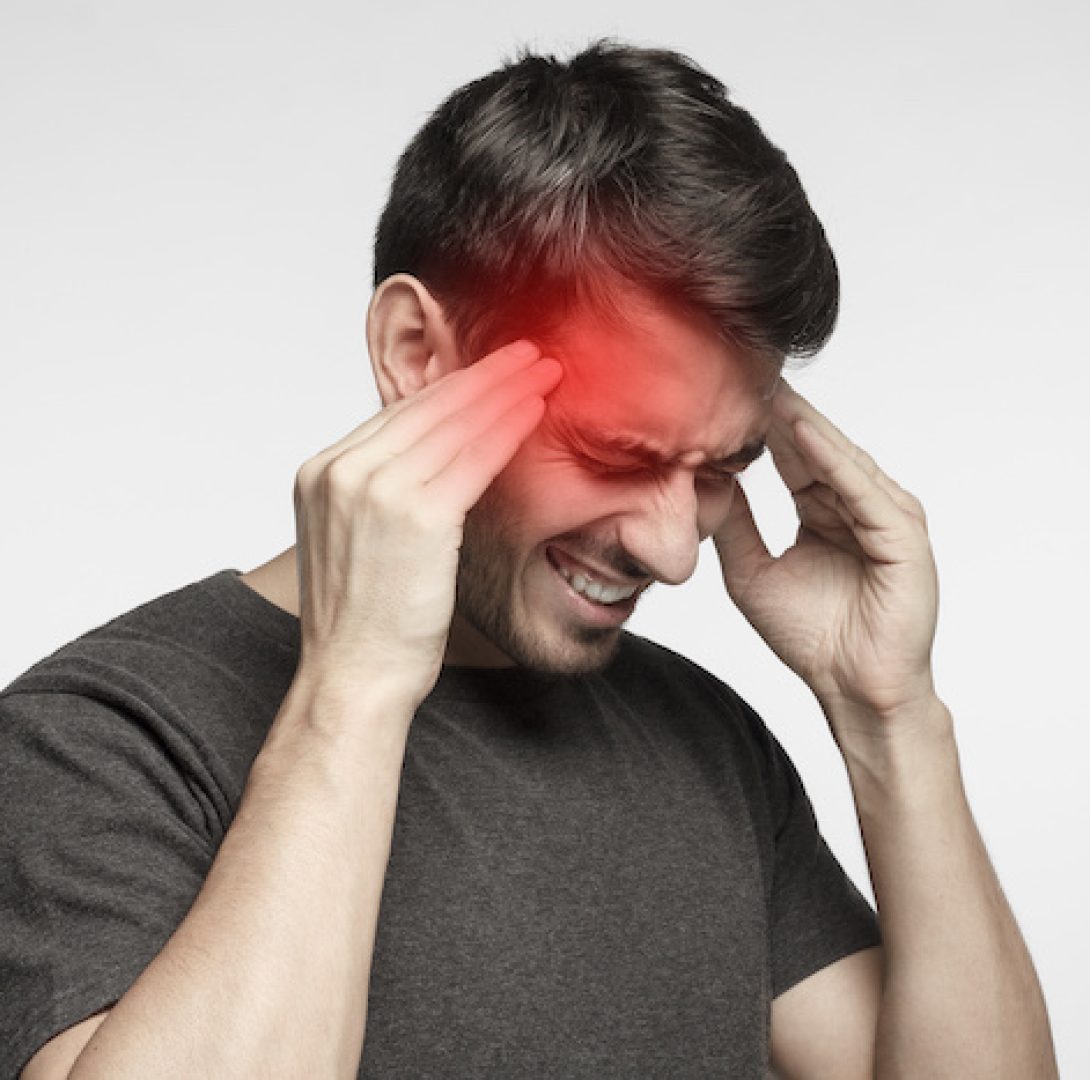 Closeup of young man touching temples with fingers as if suffering from severe migraine, feeling sick, isolated on gray background